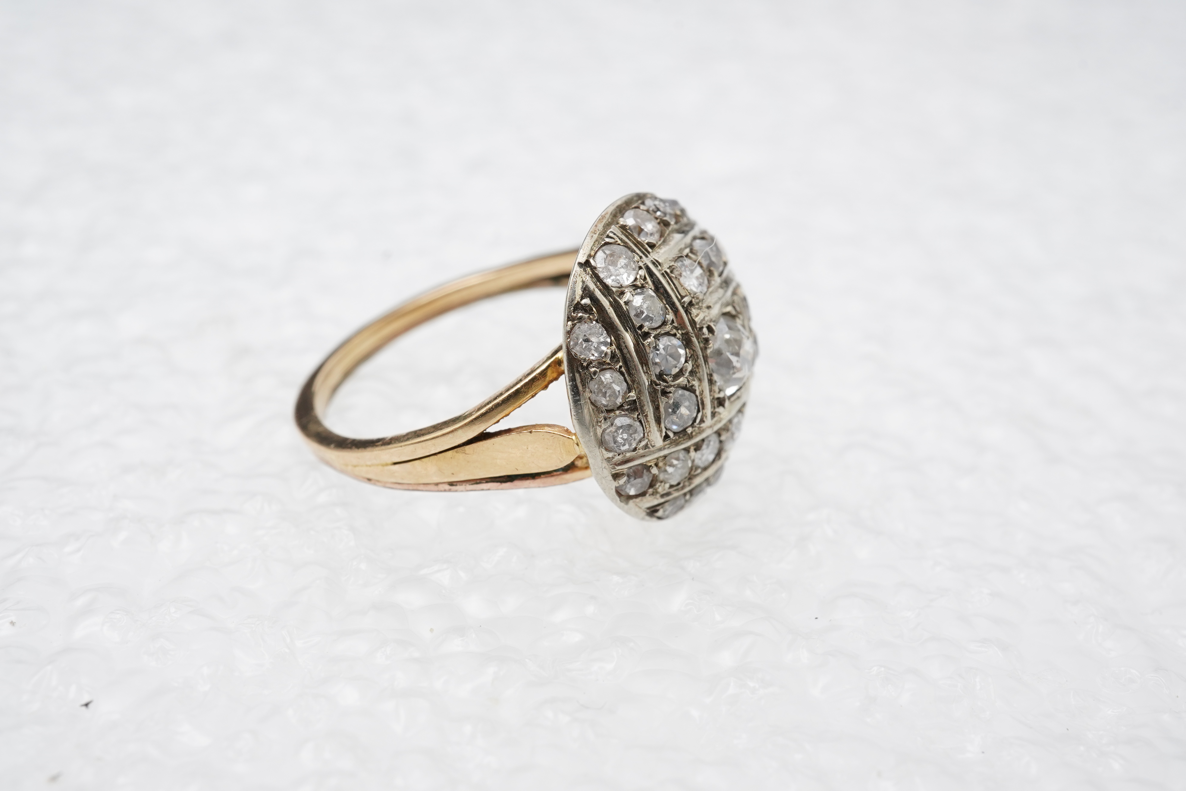 A diamond ring, centring on a circular motif of bombé design, set with geometric arrangements of cushion-shaped, single- and circular-cut diamonds totalling approximately 0.90 carats, to a gold band, size M1/2, indistinc